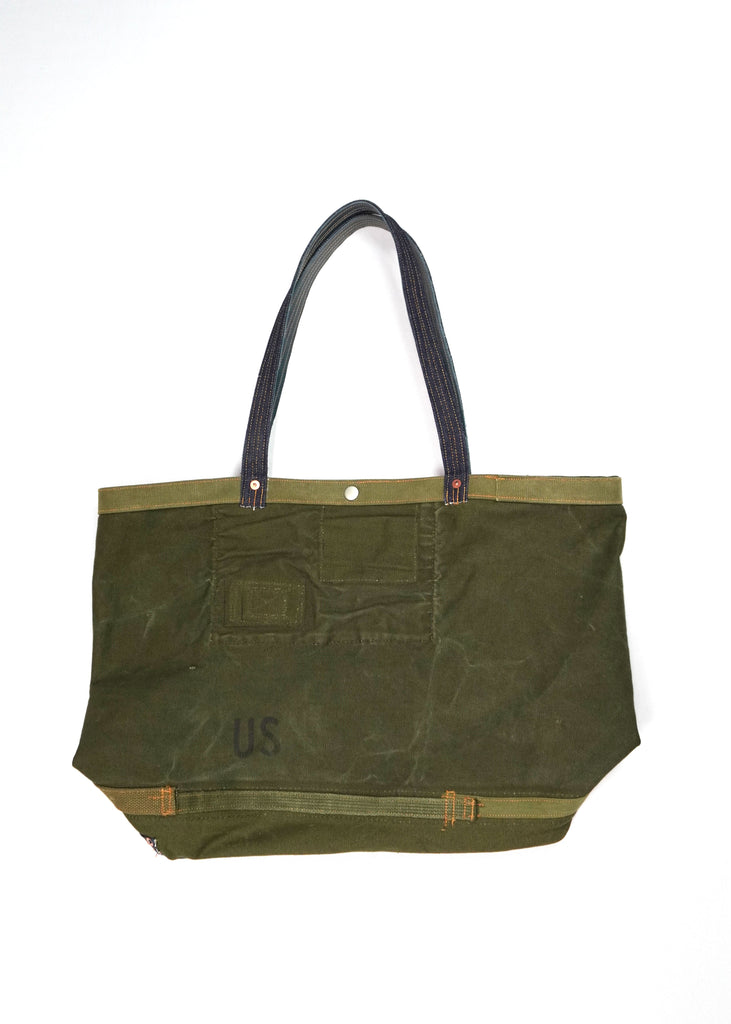 The First Standard Duffle Tote Bag 82924 is a durable and versatile carryall crafted with high-quality materials. Designed in a rugged olive-green waxed canvas, it features contrast stitching and reinforced denim handles for comfortable and sturdy handling. The exterior is adorned with a First Standard Co. logo patch for a vintage-inspired aesthetic.

A front pocket with secure stitching adds extra utility, while copper rivet accents ensure longevity. 