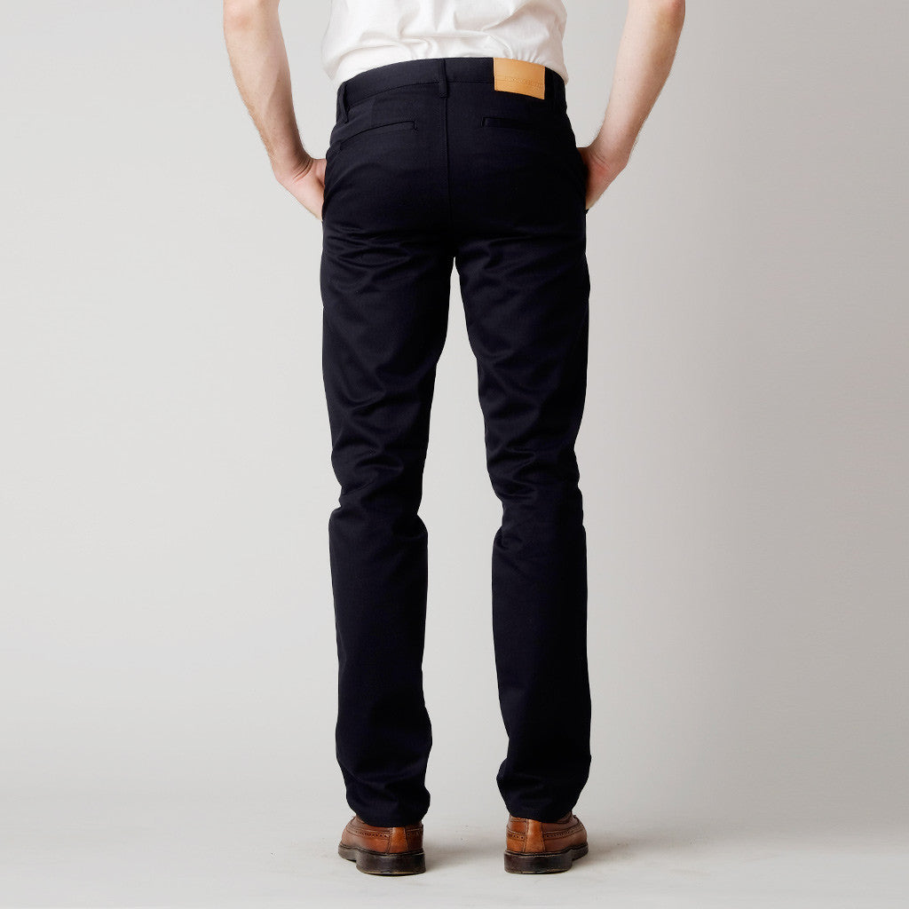Rear of slim-fit black chinos by made in the USA clothing brand Brooklyn Denim Co. Our men's chinos are pants made in the USA of 100% cotton. They feature a slimming fit throughout the leg with side pockets and slit back pockets.

Customize the fit with complimentary hemming.

100% Cotton
Slim Fit
Zipper Fly
Made in USA
Colors: Sand, Black, Jalapeño Navy